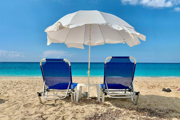 Two dark blue beach loungers with white umbrella and small table on the beach