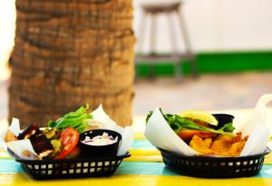 Platters of food in Plate and Parchment Paper Liners on picnic table in front of a palm tree