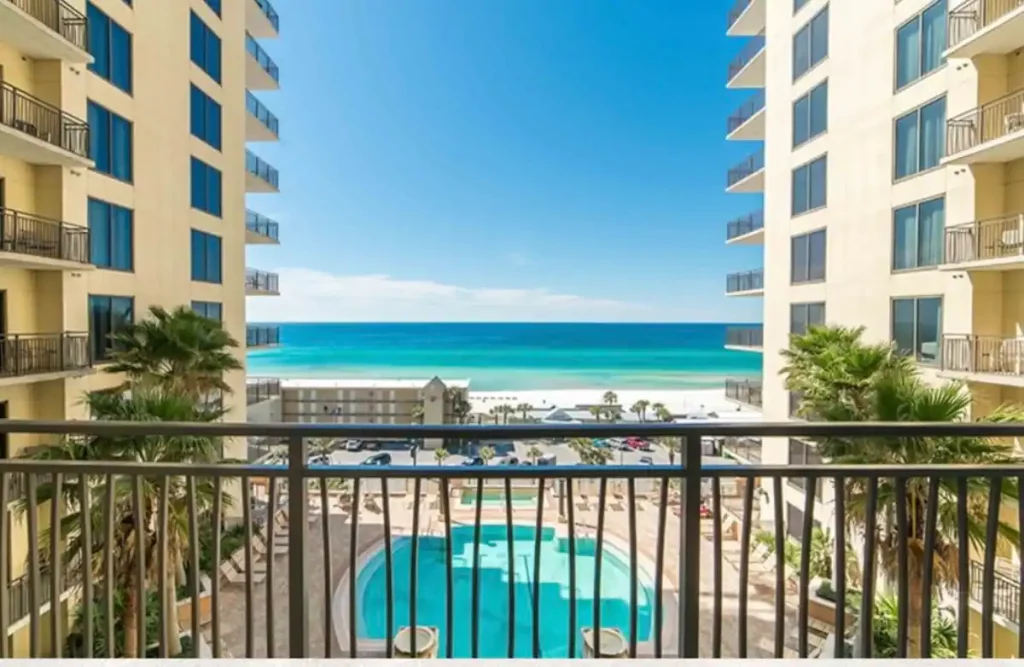 Two hotel towers of a pool and hot tub with beach view in the background