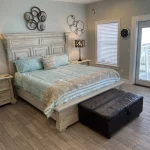 Main bedroom with bed and nightstands. There's an otteman at the end of the bed as well as circular decorations on the wall