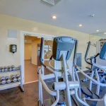 Yellow workout room with wall of mirrors and various workout equipment