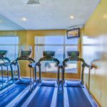 Yellow workout room with wall of mirrors and three treadmills