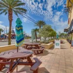 View of a street in a beachy town with palm trees, picnic tables, and a Starbucks