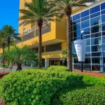 Exterior of a yellow building with a glass wall and tropical landscaping