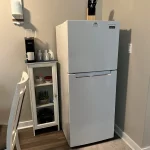 A coffee maker set up on a narrow cabinet next to a fridge with a knife set on top