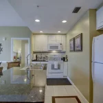 Long narrow kitchen with white cabinets and appliances and stone counters