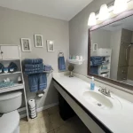 A bathroom with a large counter top, mirror, and toilet with shelf