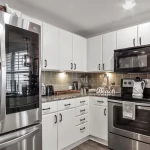 White kitchen with granite counter tops, stainless steel appliances, and a connected bar with stools