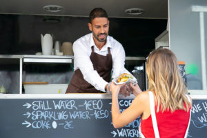 Man in a food truck handing a woman a sandwich