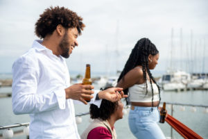 Young black adults laughing and drinking beer on a boat looking out on the water