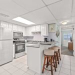 White kitchen with gray counter and stainless steel appliances with bar and stools