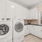 Large laundry room with white washer and dryer and cabinets surrounding them